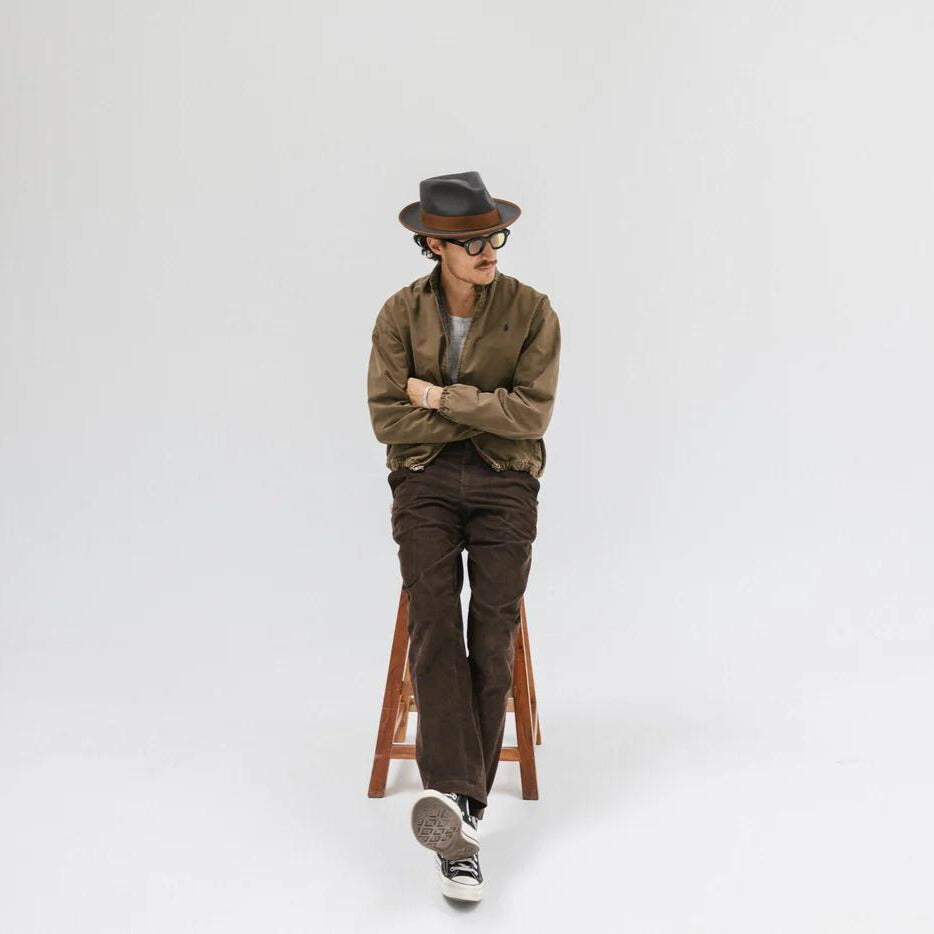 Man looking into a circle mirror wearing a tan felt men’s casual hat with jeans and a linen button-up shirt