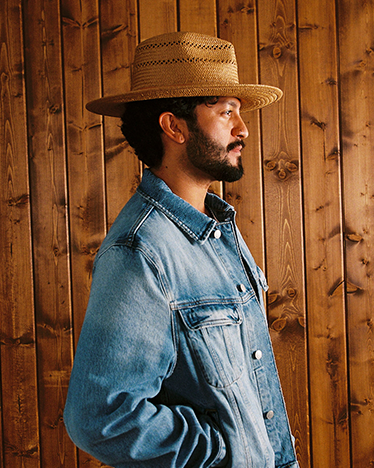 Man wearing a straw hat and denim jacket against a wooden background