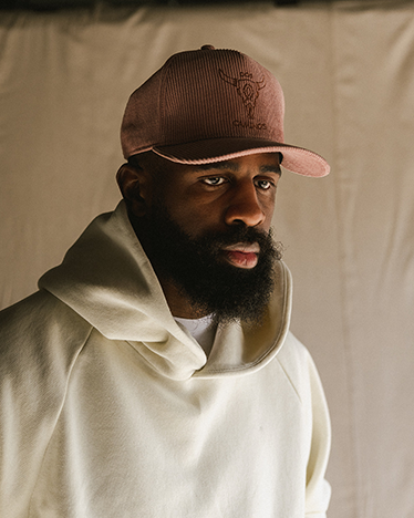Man wearing a brown cap and white hoodie against a beige background
