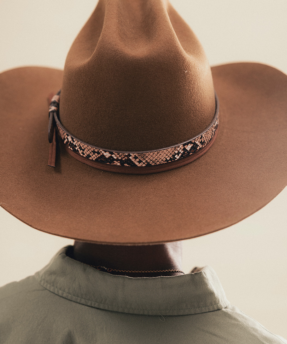 A close-up shot of a person from behind wearing a brown felt cowboy hat with a decorative patterned leather band and a light olive green shirt collar #color_brown