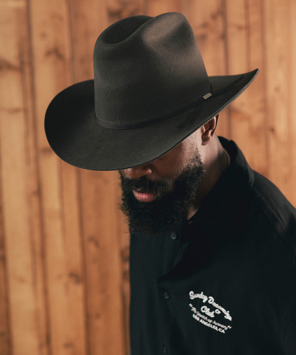 Man wearing a black cowboy hat and black shirt with a logo against a wooden background #color_hickory