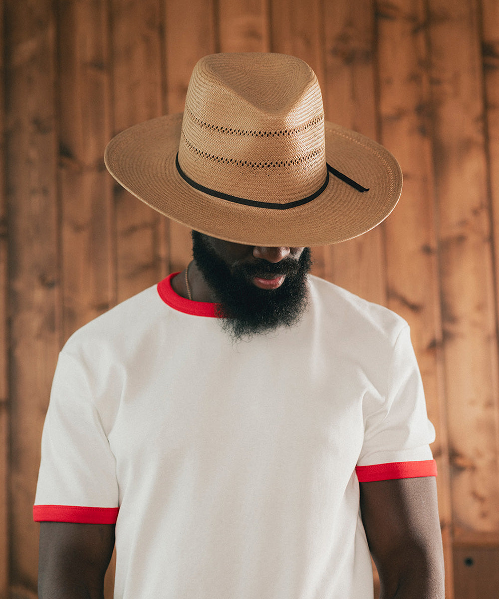 Man wearing a straw hat and white shirt with red trim against a wooden background #color_natural