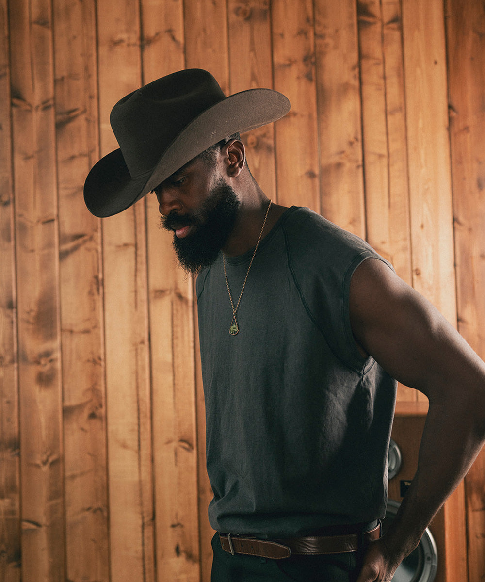 Man wearing a cowboy hat and sleeveless shirt against a wooden wall #color_hickory
