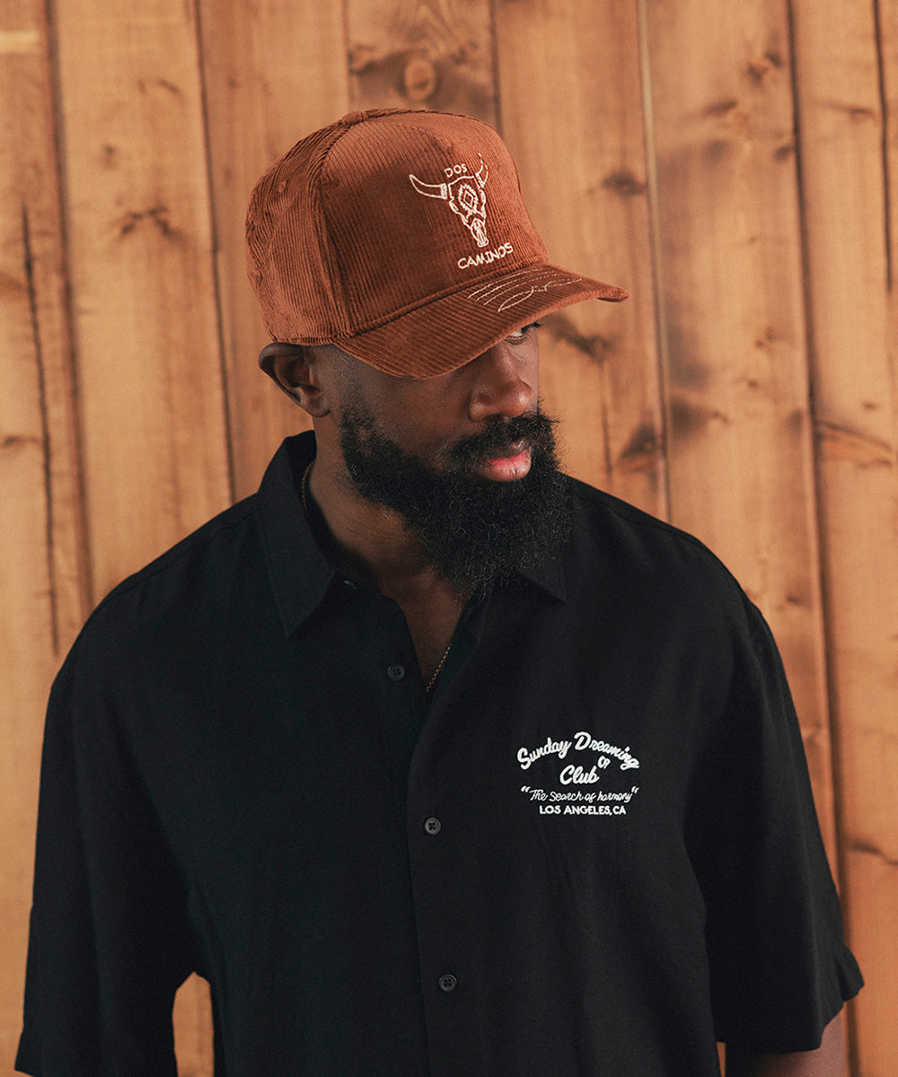 Man wearing a black shirt and brown cap with branding against a wooden background #color_sienna