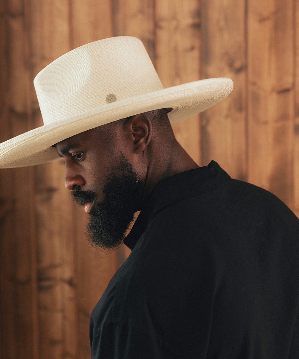 Man wearing a wide-brimmed beige hat against a wooden background #color_ivory