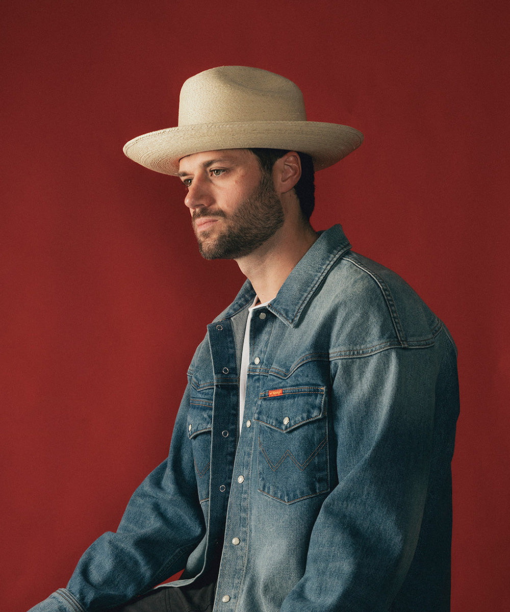 Man wearing a beige hat and blue denim jacket against a red background #color_ivory