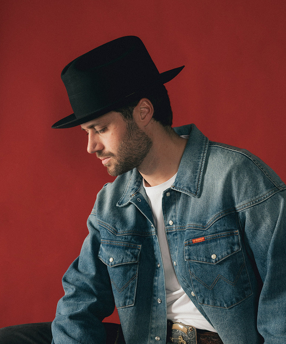 Man wearing a black hat and blue denim jacket against a red background #color_black