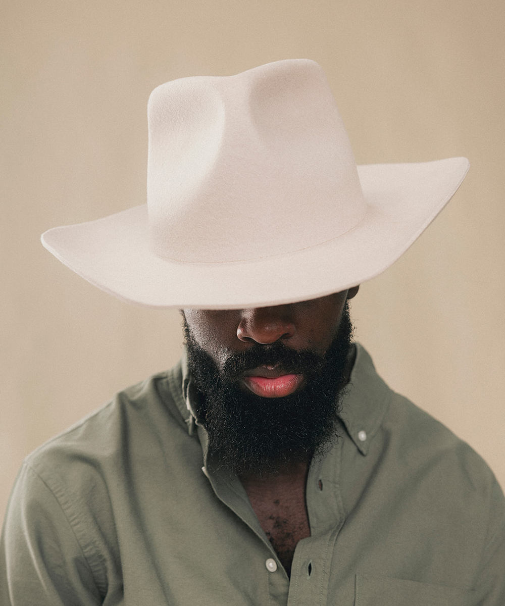 A man wearing a wide-brimmed cream cowboy hat and an olive green button-down shirt, photographed against a solid beige background #color_silverbelly