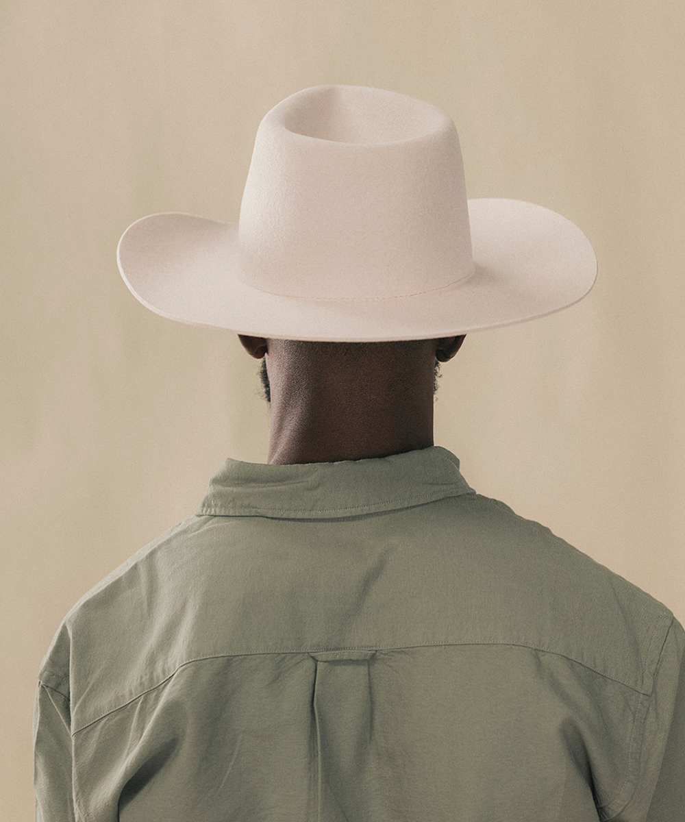 A man wearing a wide-brimmed cream cowboy hat and an olive green button-down shirt, photographed against a solid beige background #color_silverbelly