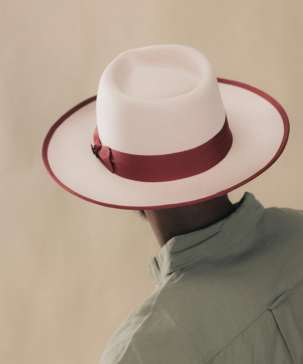 A white felt fedora hat with a dark red ribbon band, worn by a person shown from behind against a plain beige background #color_maroon