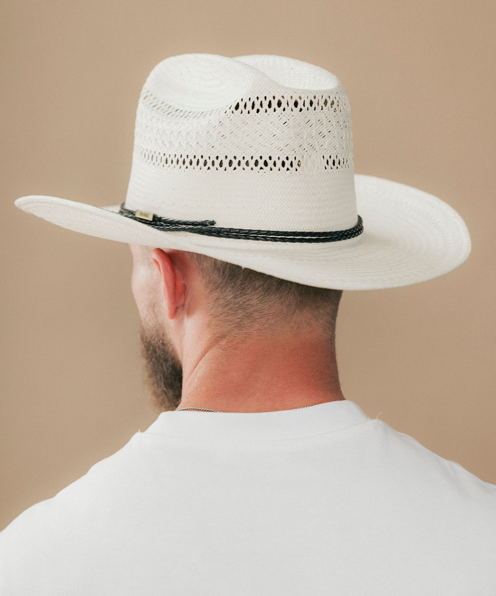 A man viewed from behind wearing a white woven cowboy hat with a dark braided band, against a plain beige background #color_ivory