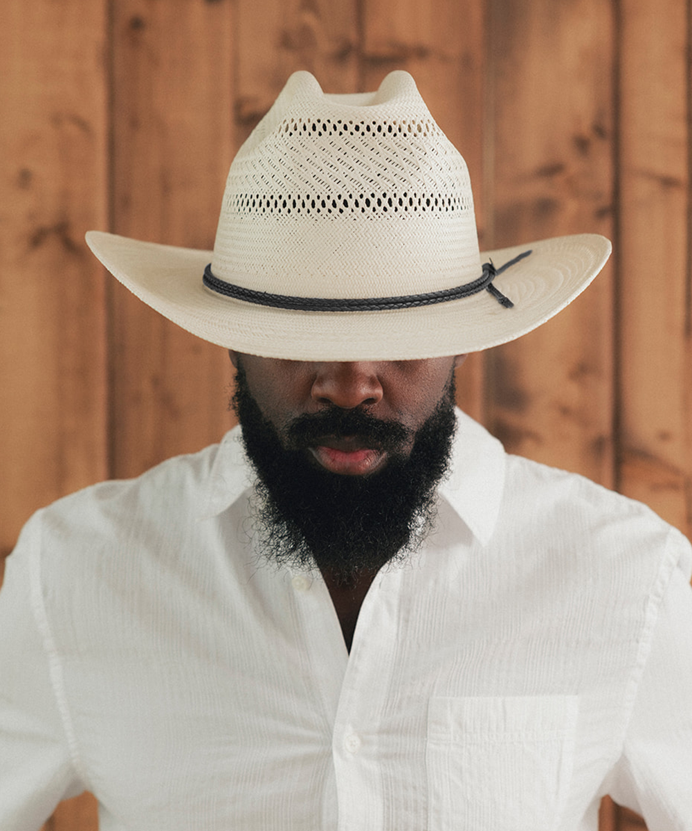 Man wearing a white cowboy hat and white shirt against a wooden background #color_ivory