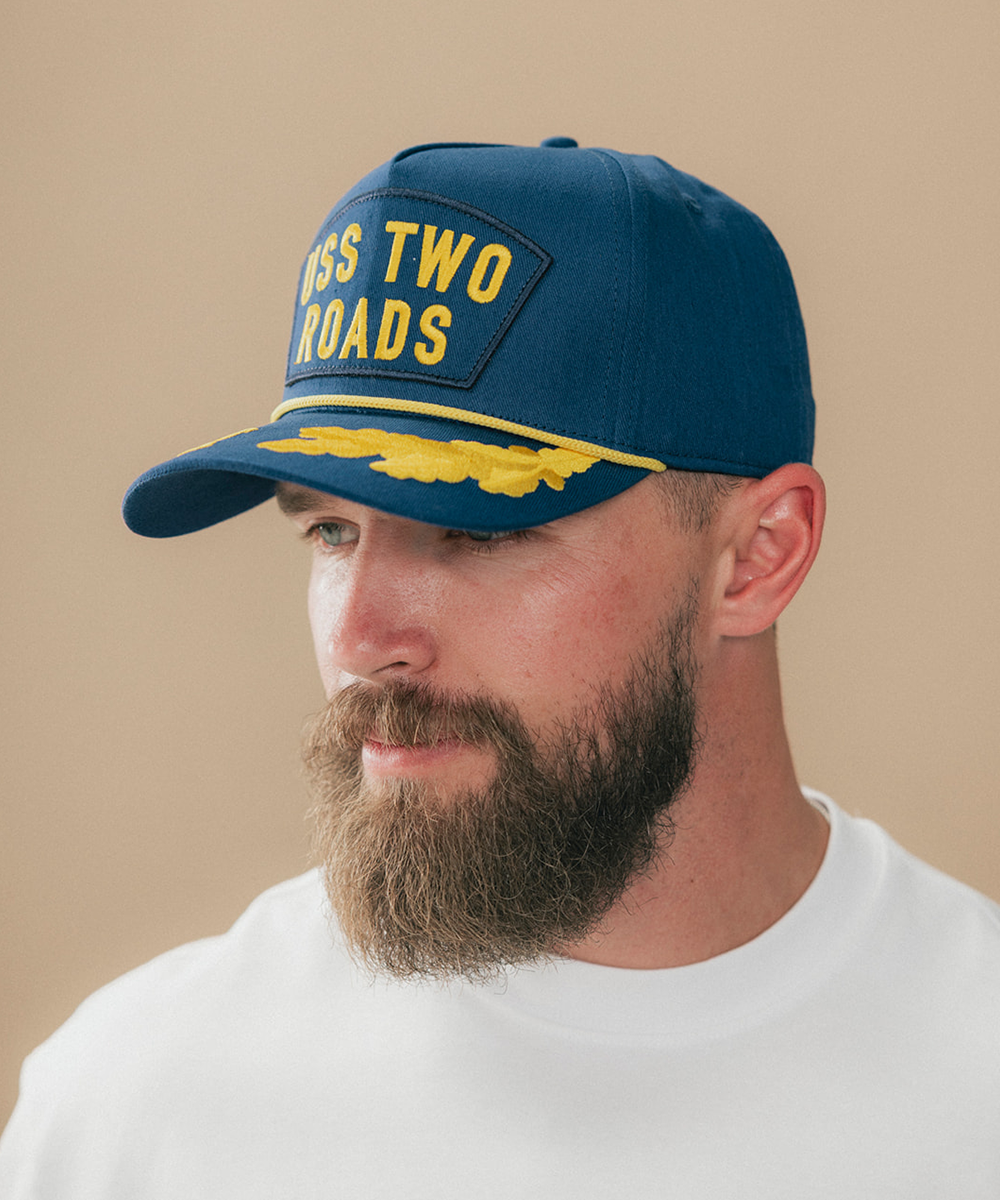 A man wearing a navy blue baseball cap with yellow embroidered text #color_blue
