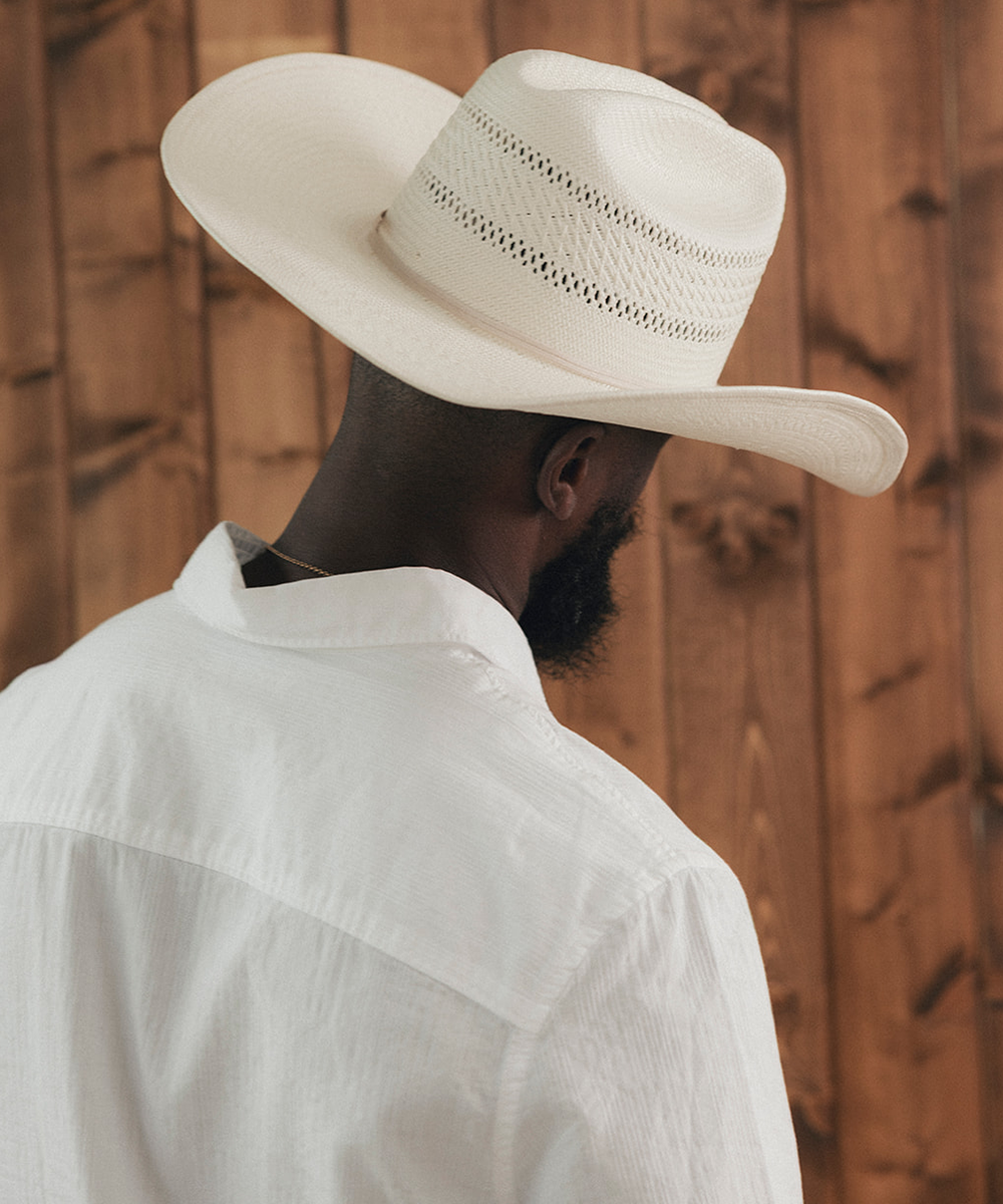 Man wearing a wide-brimmed white hat against a wooden background #color_ivory