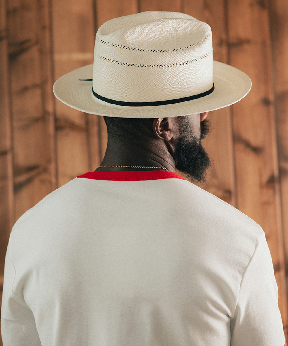 Man wearing a white Panama hat with a wooden background #color_off white