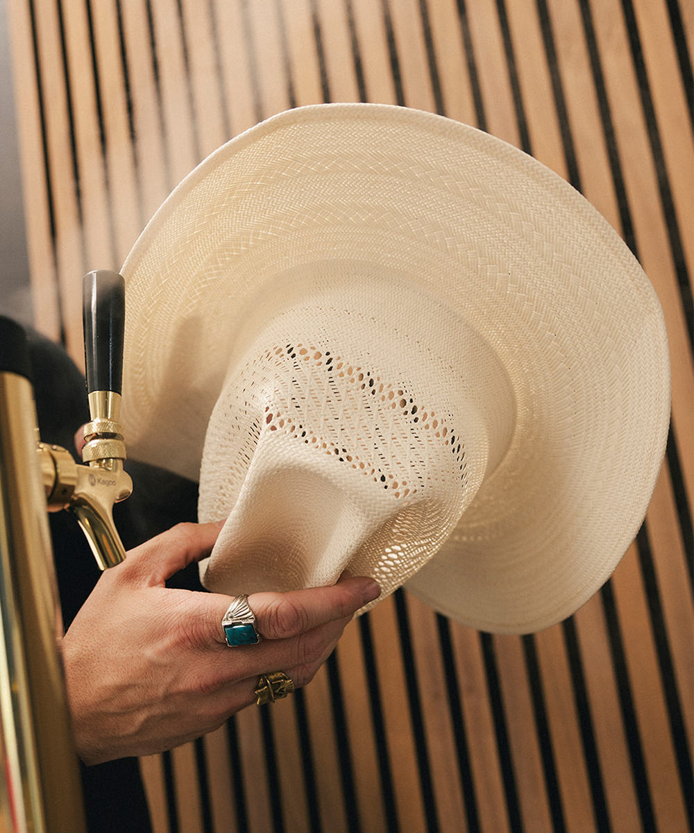 Person holding a white straw hat with a wooden background #color_ivory