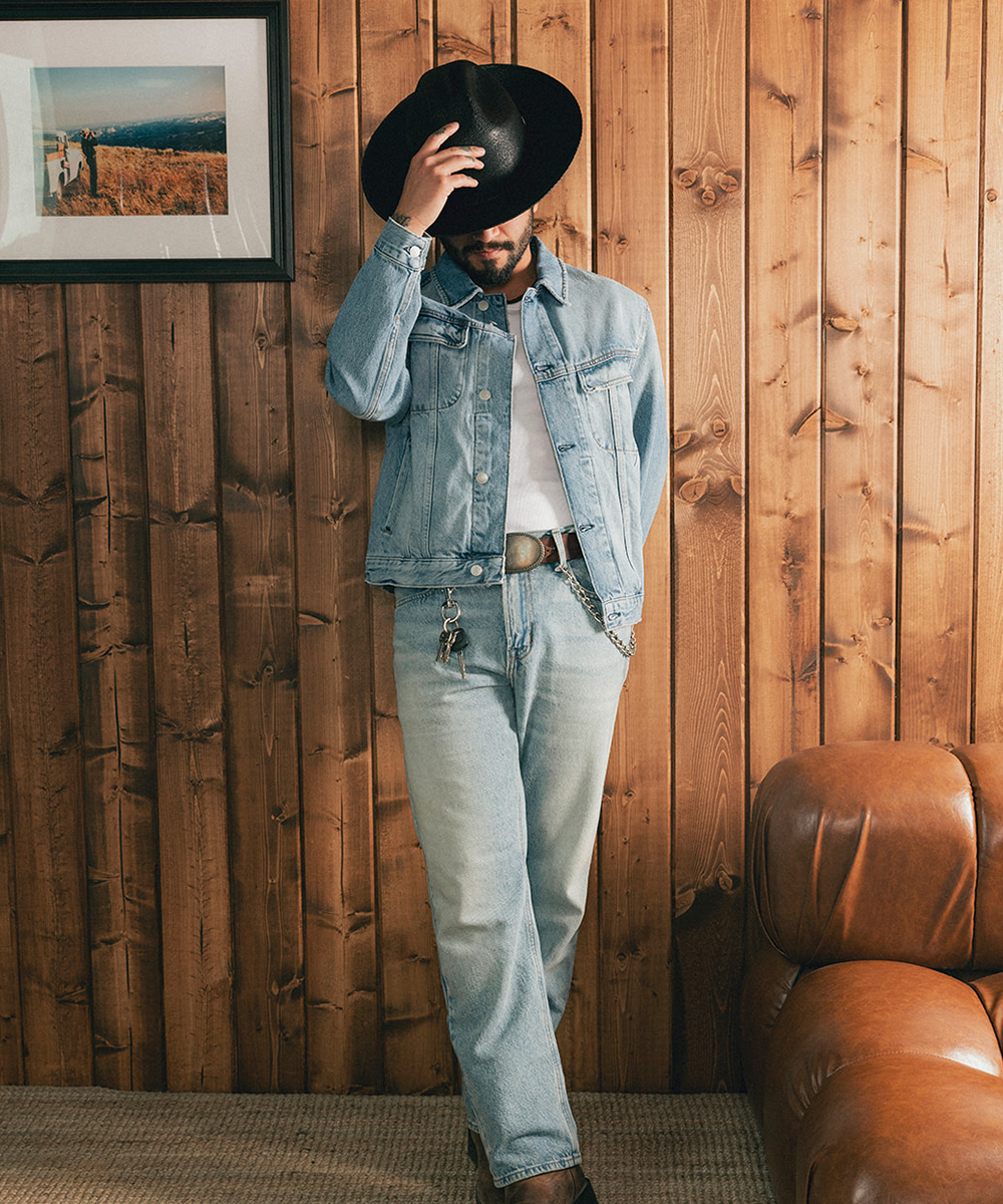 Man wearing a black straw hat and denim jacket against a wooden wall #color_black