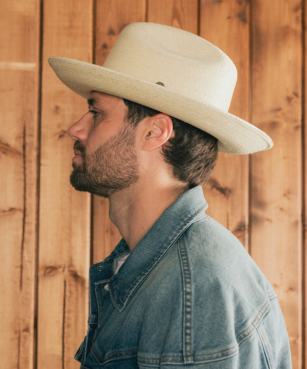 Man wearing an ivory straw hat and denim jacket against a wooden background #color_ivory