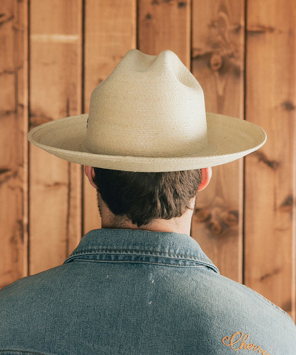 Man wearing an ivory straw hat and denim jacket against a wooden background #color_ivory