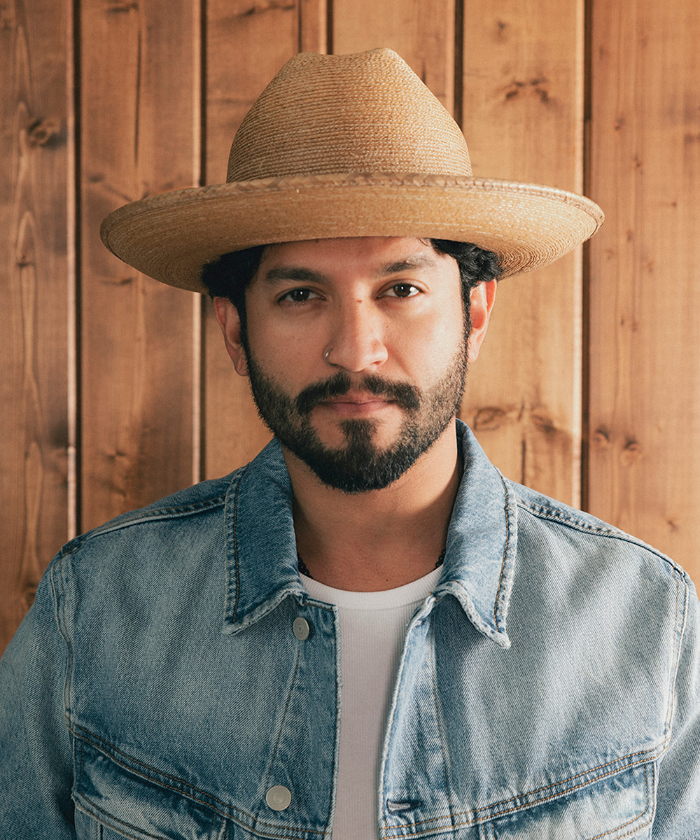 Man wearing a straw hat and denim jacket against a wooden background #color_oak