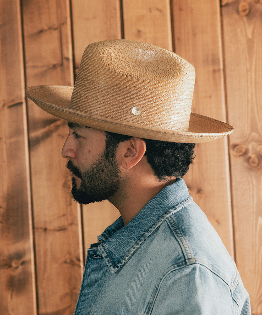 Man wearing a straw hat and denim jacket against a wooden background #color_oak