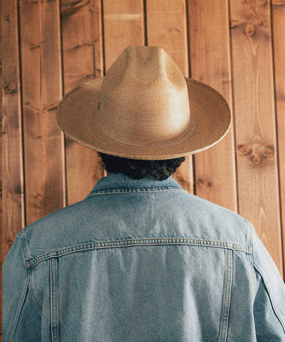 Man wearing a straw hat and denim jacket against a wooden background #color_oak
