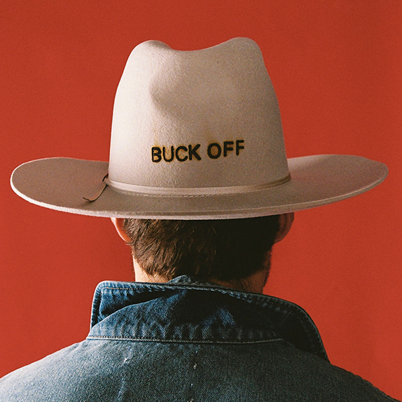 Person wearing a beige cowboy hat with 'Buck Off' text on a red background