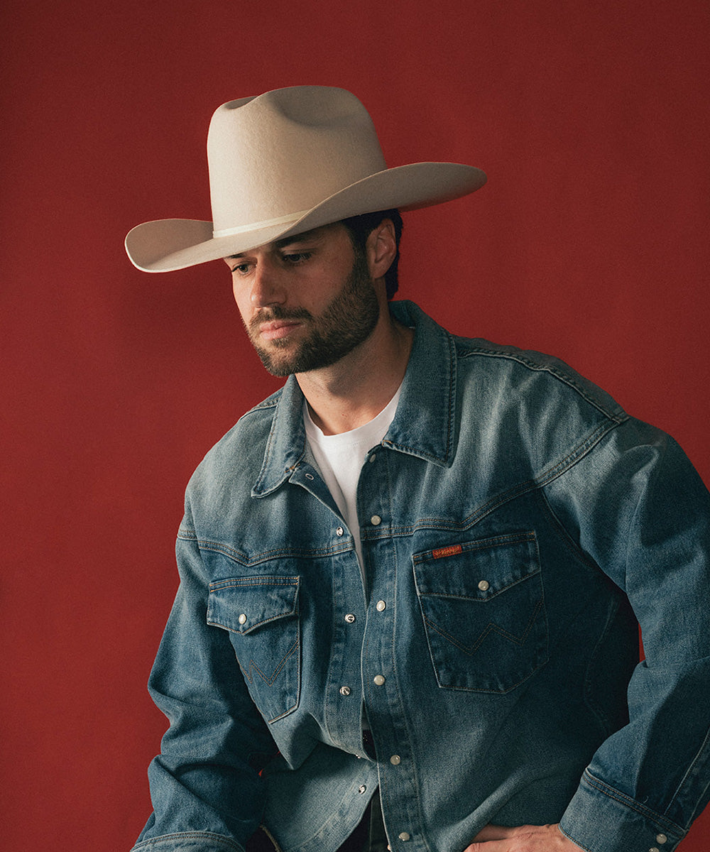 Man wearing a beige cowboy hat and denim jacket against a red background #color_buckskin