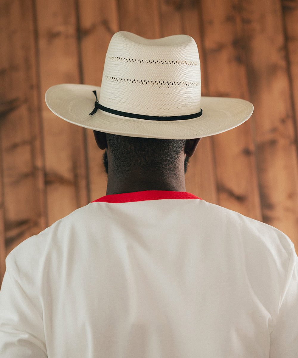 Man wearing a white straw hat and red and white shirt against a wooden background #color_ivory