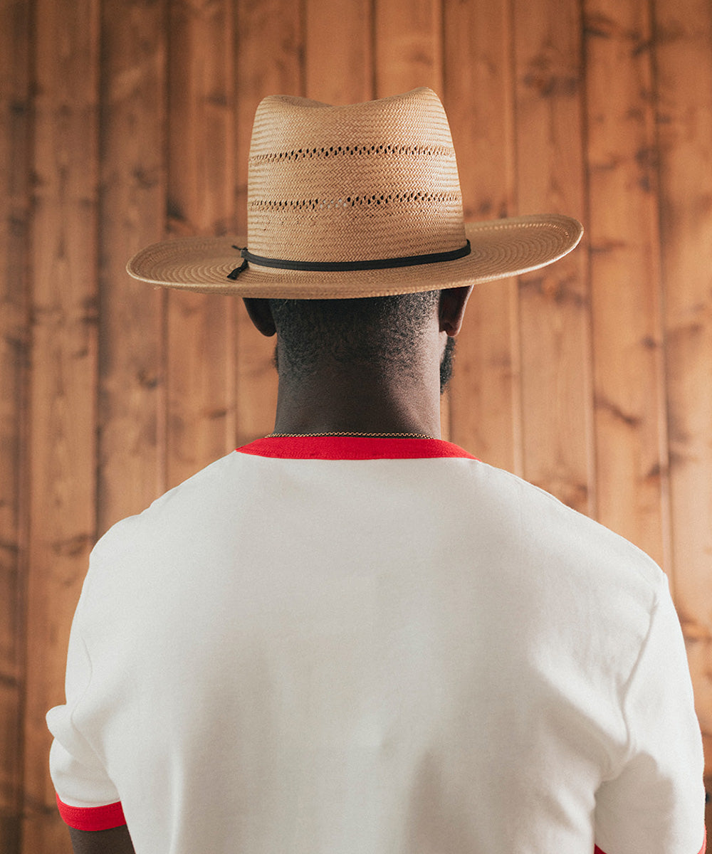Man wearing a straw hat and white shirt with red trim against a wooden background #color_natural