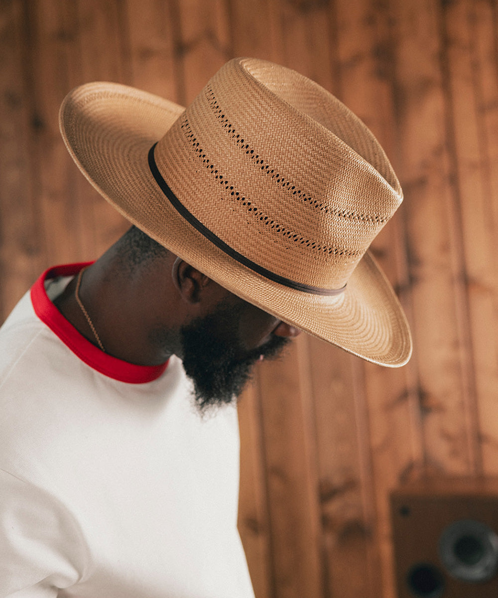 Man wearing a straw hat and white shirt with red trim against a wooden background #color_natural