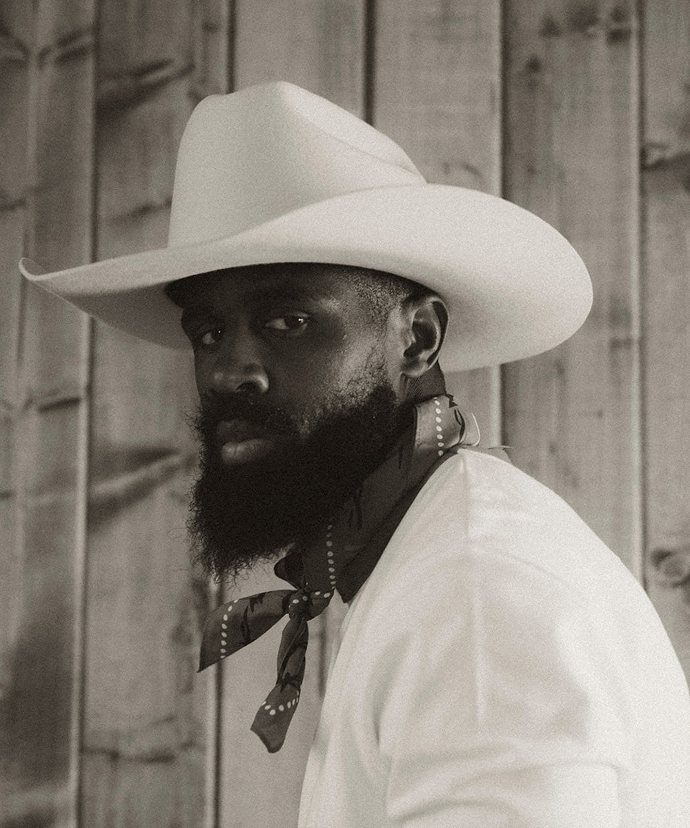 Man wearing a cowboy hat and white shirt against a wooden background #color_buckskin