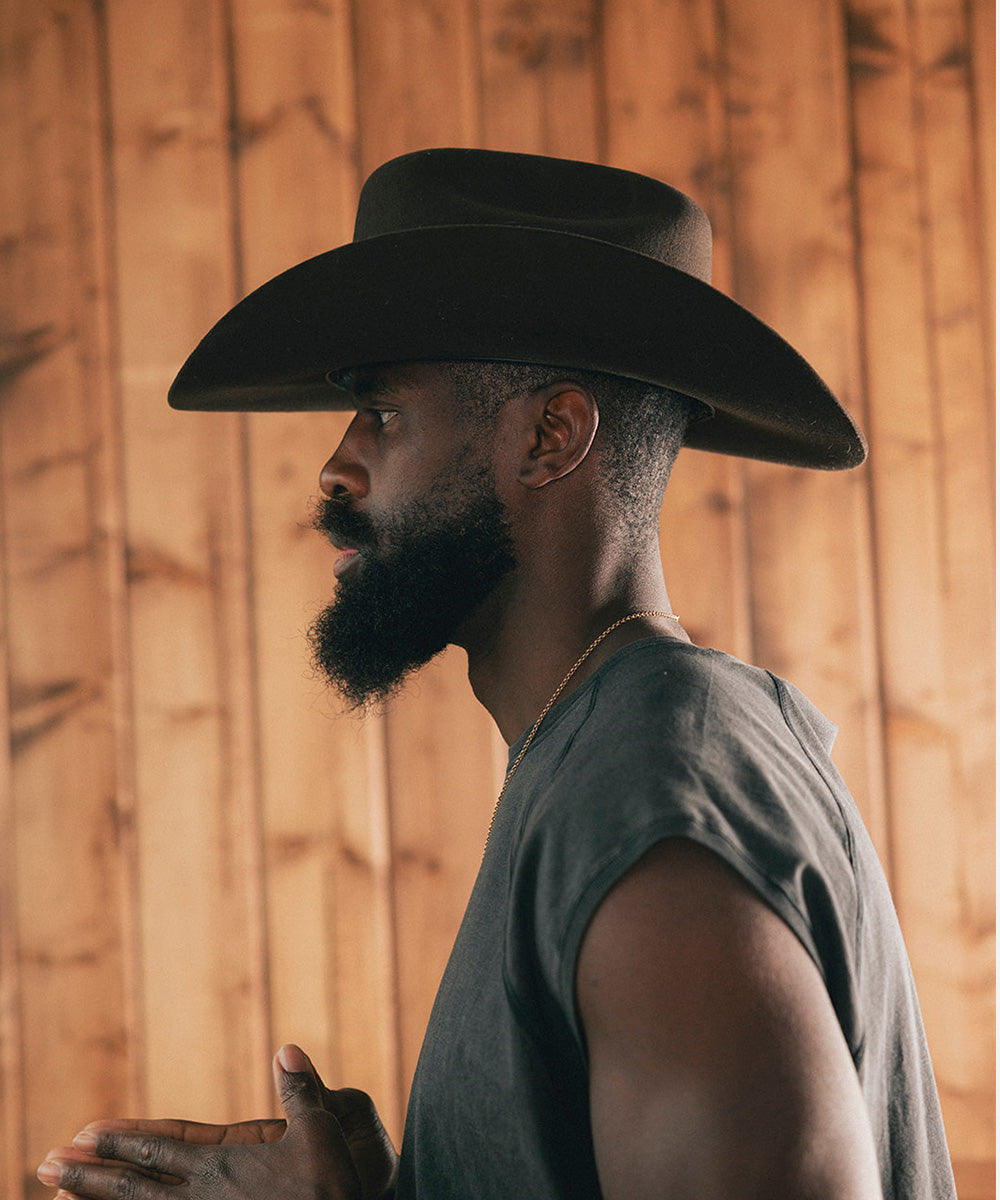 Man wearing a cowboy hat and sleeveless shirt against a wooden wall #color_hickory