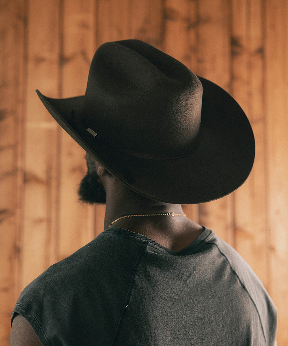 Man wearing a cowboy hat and sleeveless shirt against a wooden wall #color_hickory