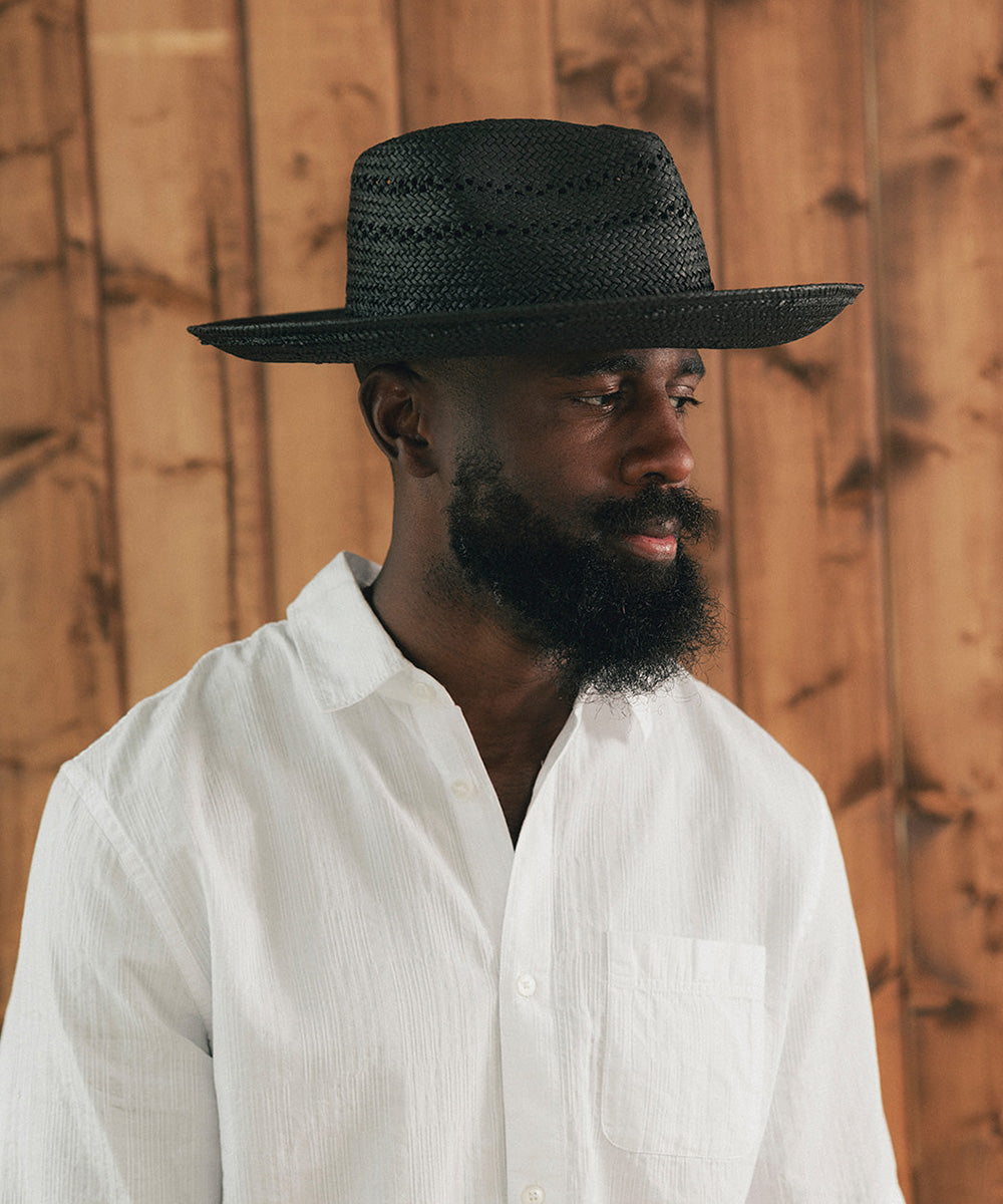 Man wearing a black straw hat and white shirt against a wooden background #color_black