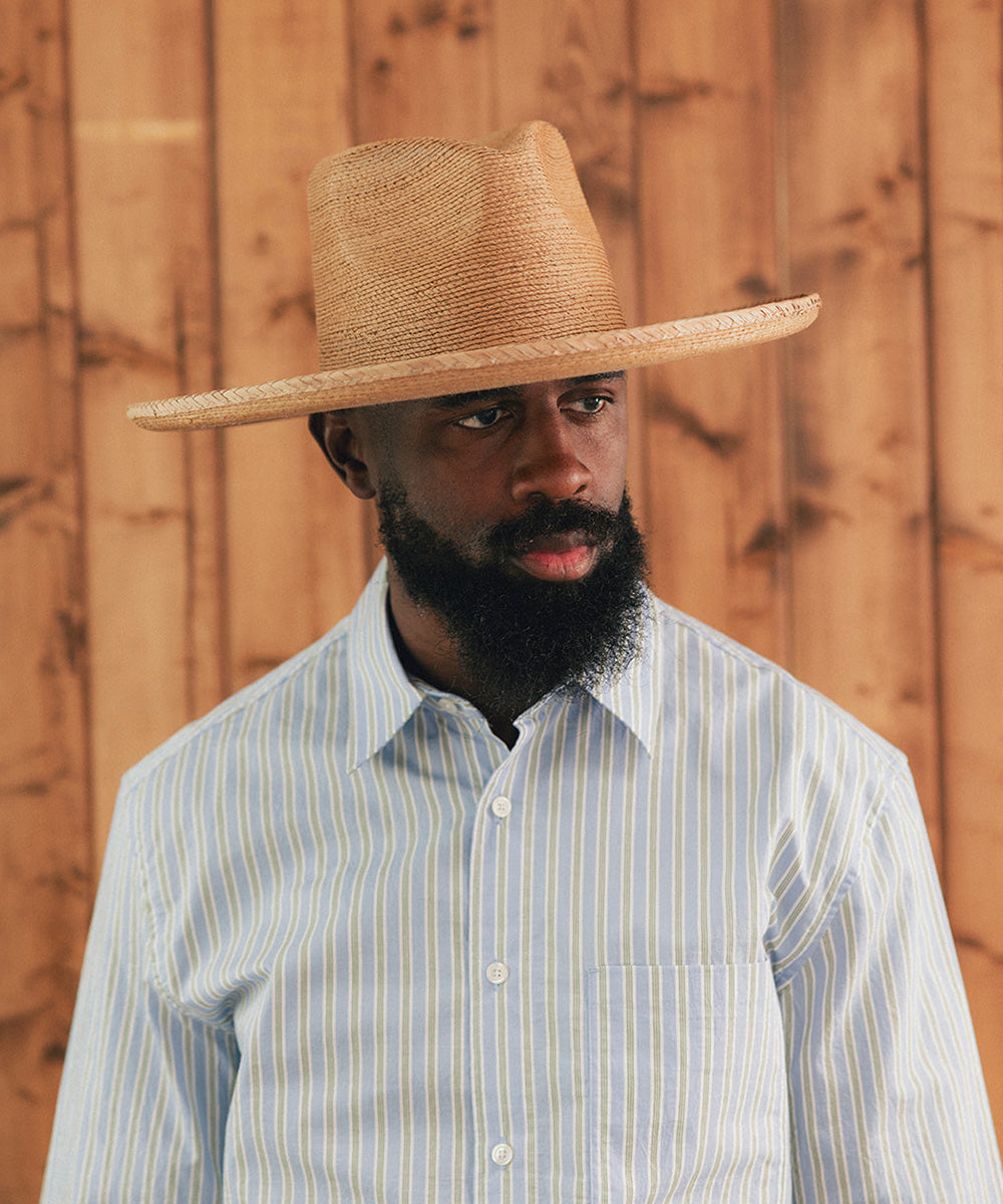 Man wearing a straw hat and striped shirt against a wooden background #color_oak