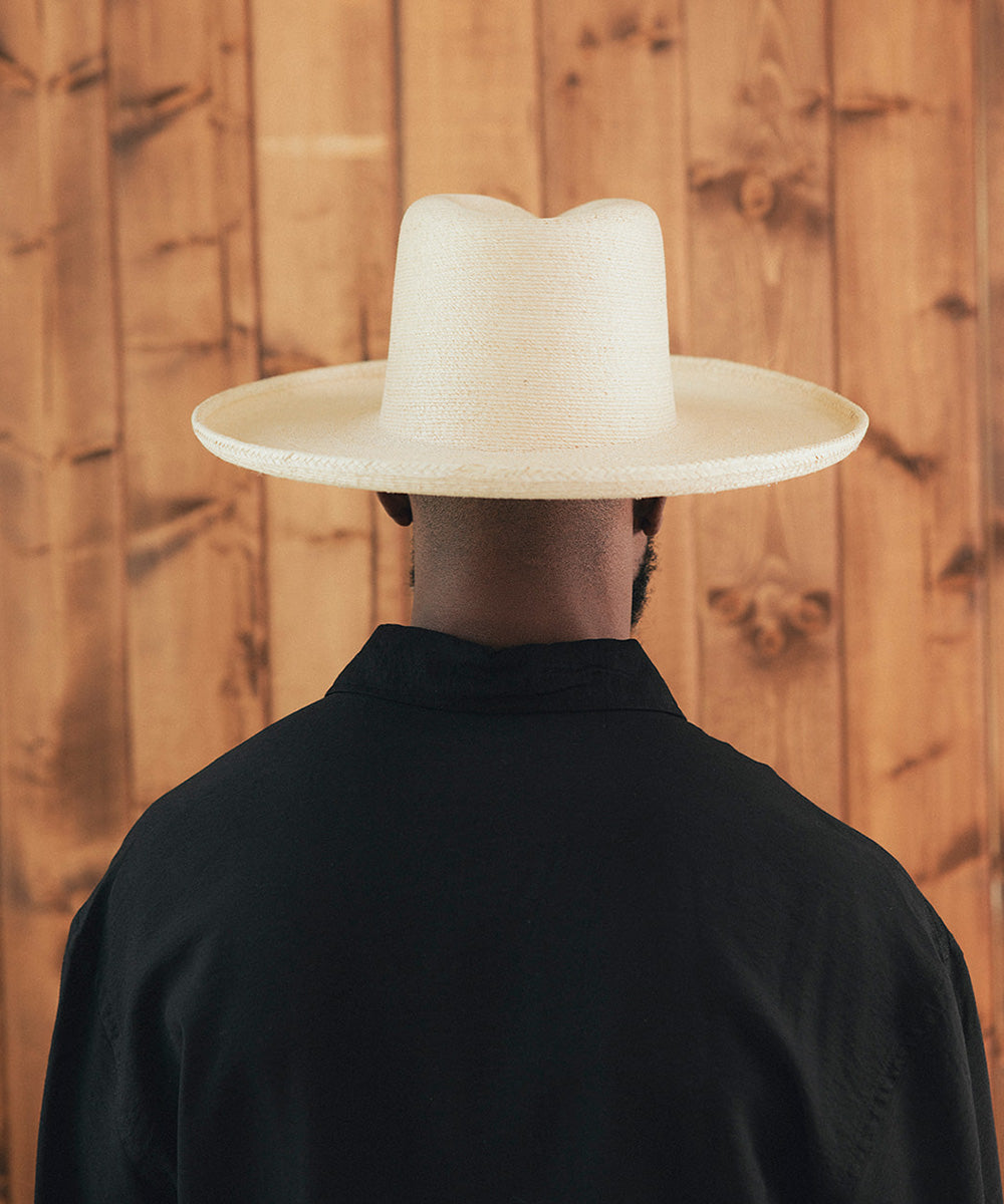 Man wearing a wide-brimmed beige hat against a wooden background #color_ivory