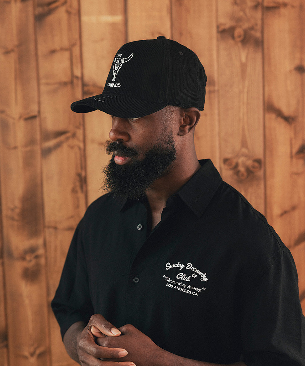 Man wearing a black cap and black shirt against a wooden wall #color_black