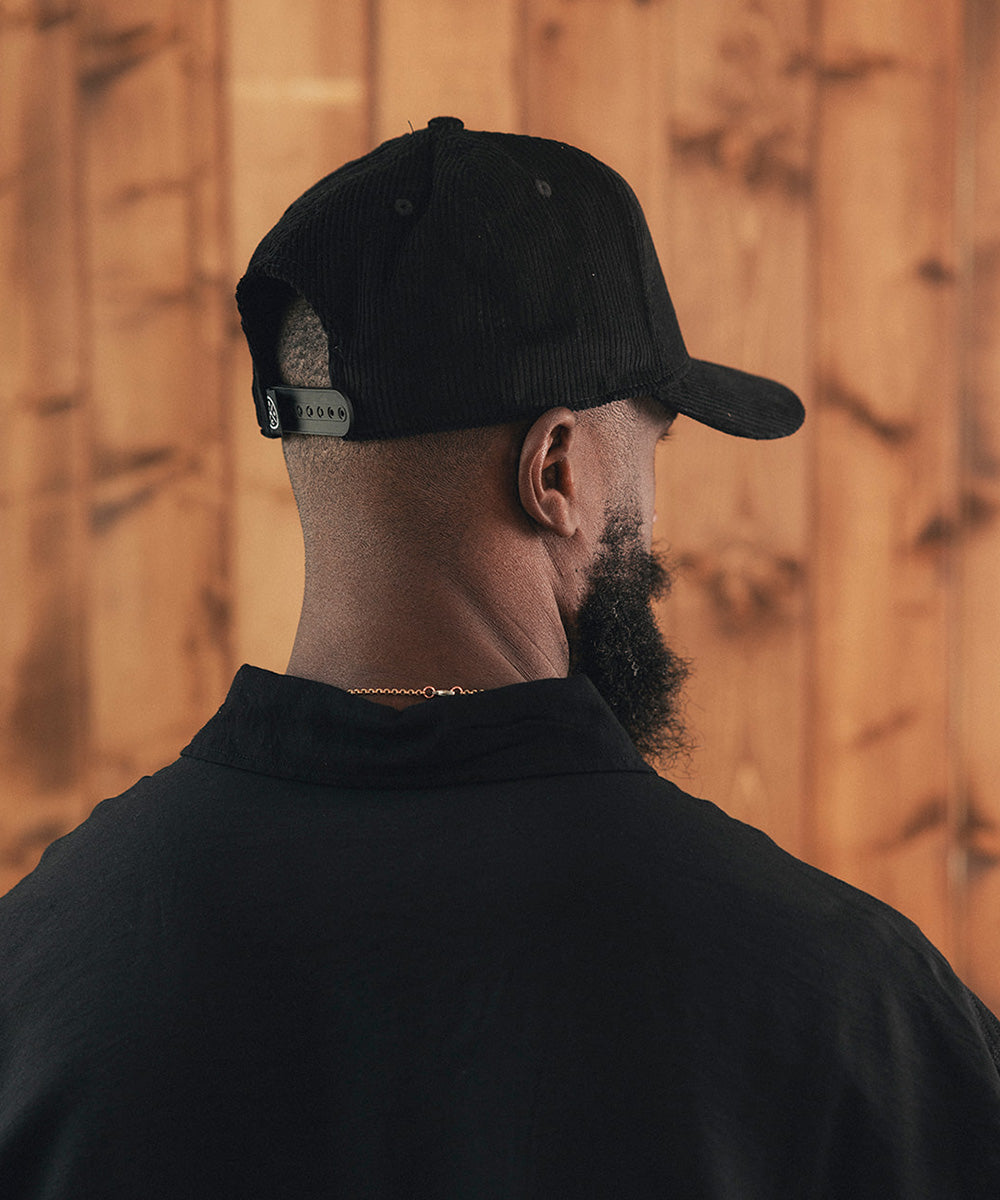Man wearing a black cap and black shirt against a wooden wall #color_black
