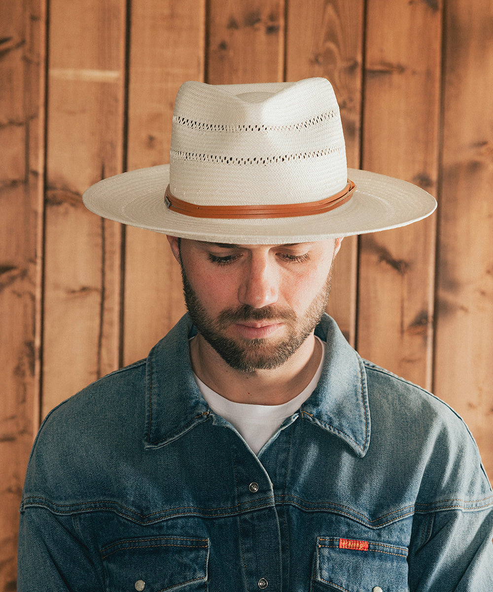 Man wearing a white straw hat with a brown band against a wooden background #color_ivory