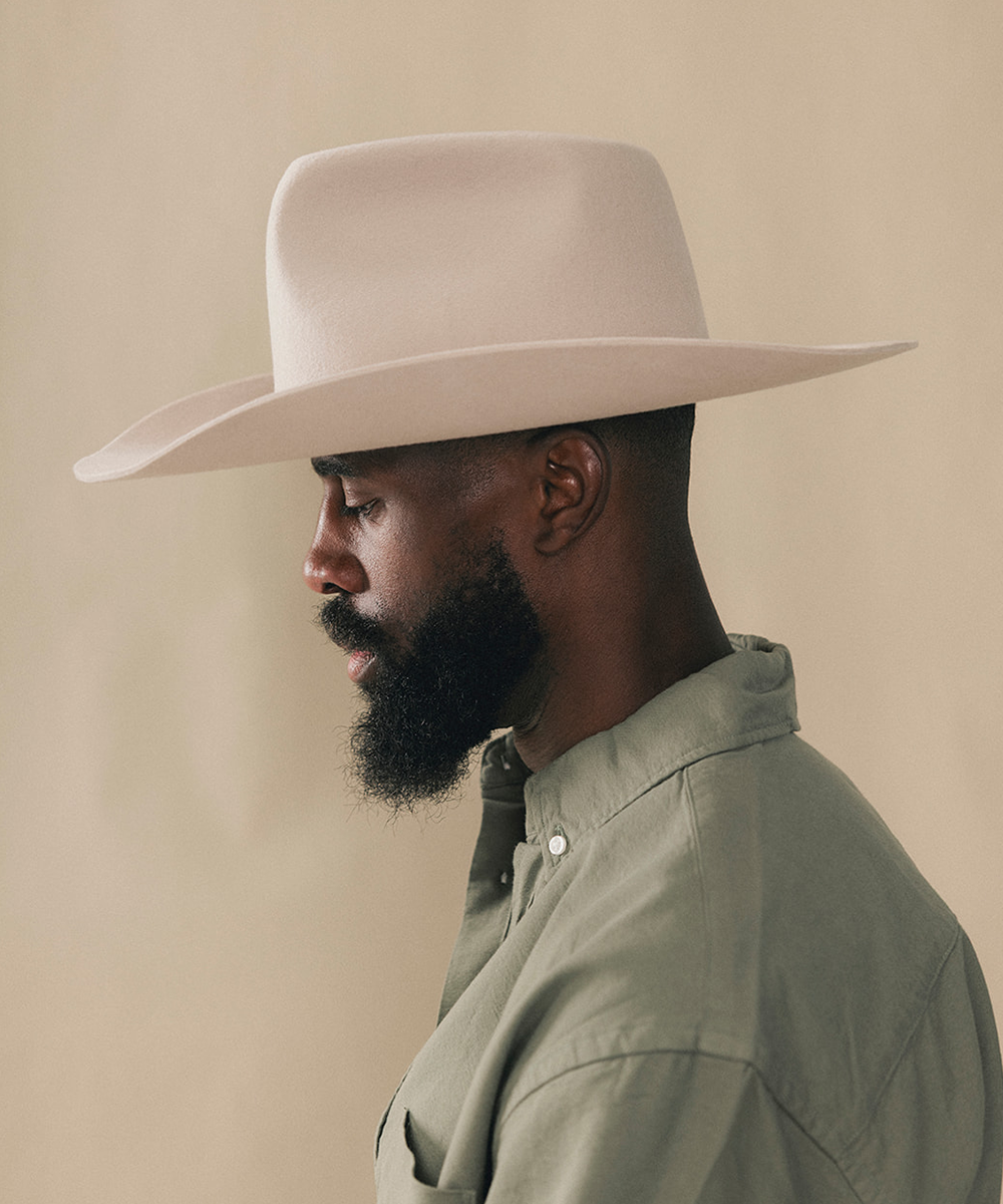 A man wearing a wide-brimmed cream cowboy hat and an olive green button-down shirt, photographed against a solid beige background #color_silverbelly