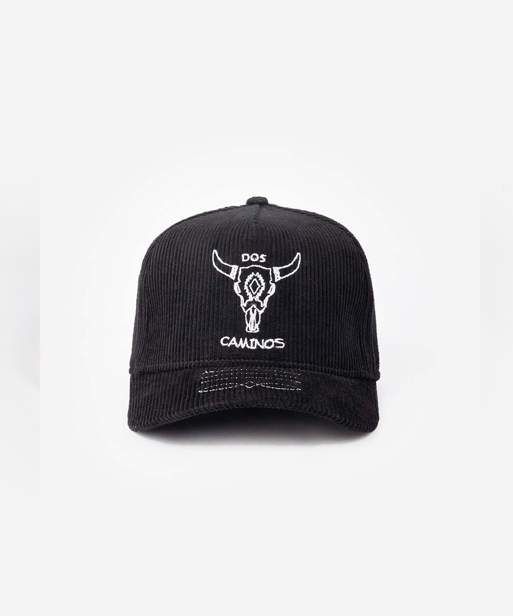 A black corduroy baseball cap with a white embroidered bull skull logo and the text 'DOS CAMINOS' on the front, set against a plain white background #color_obsidian