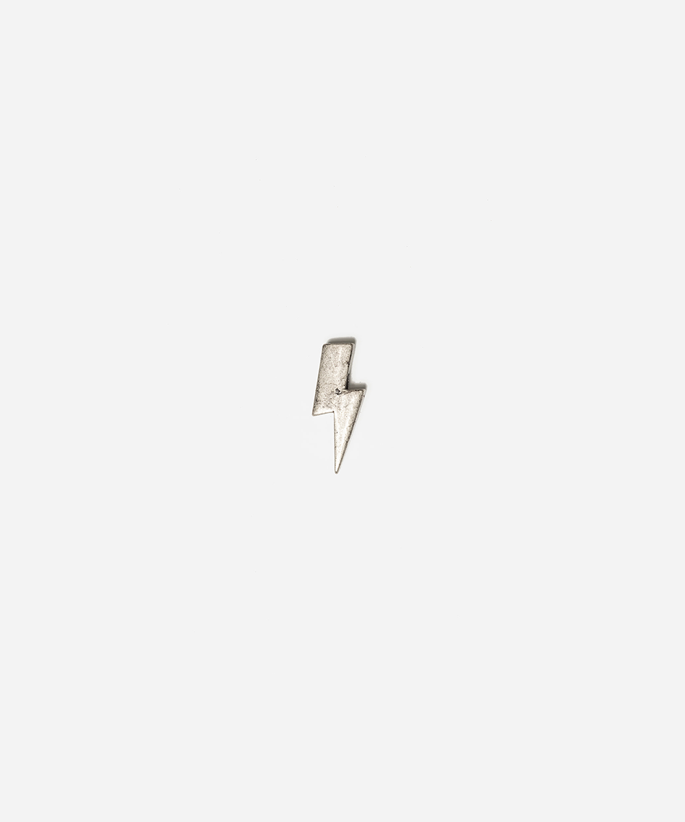 A small silver lightning bolt charm or pendant centered on a plain light gray background #color_anti silver