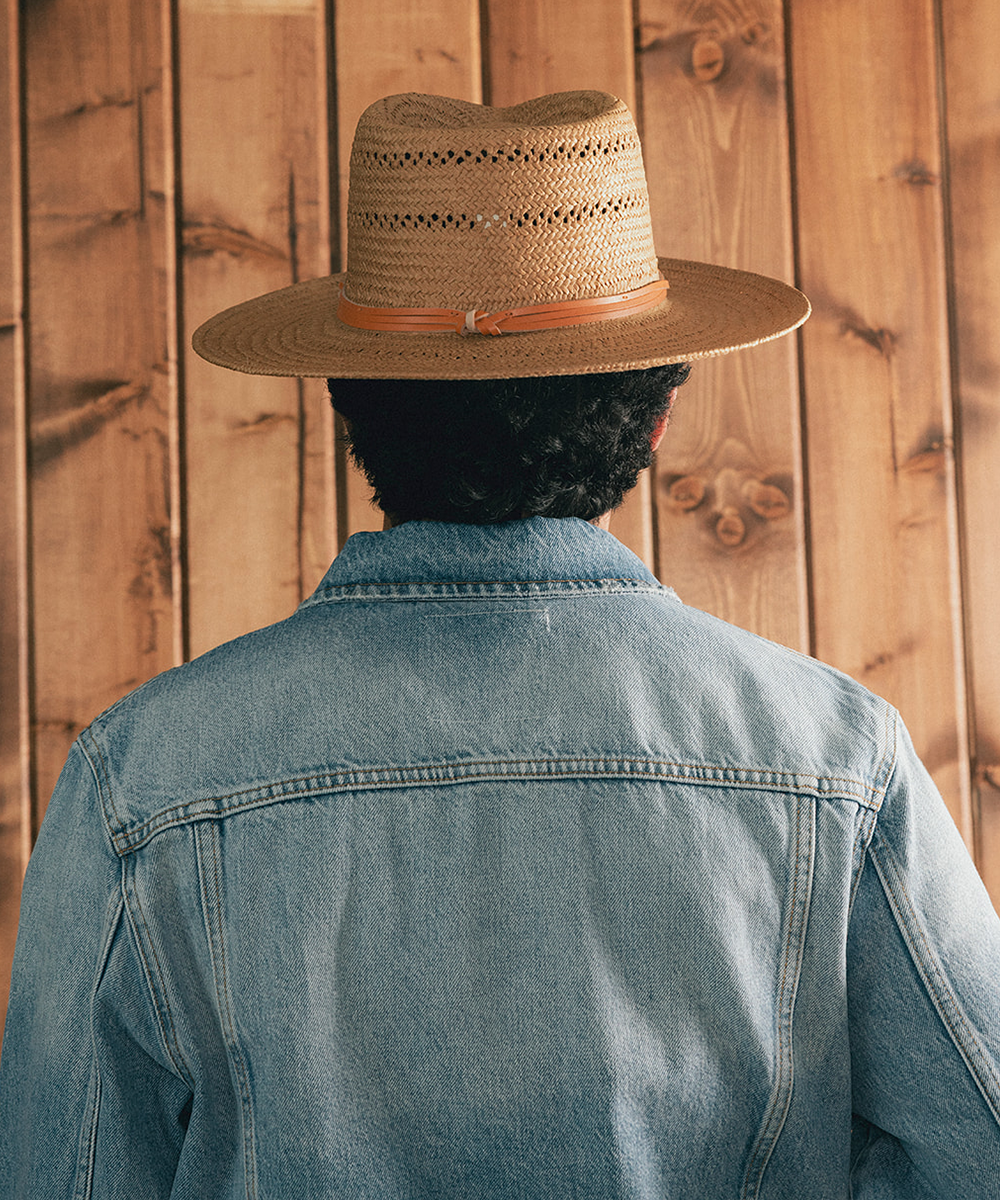 Man wearing a straw hat and denim jacket against a wooden background #color_natural
