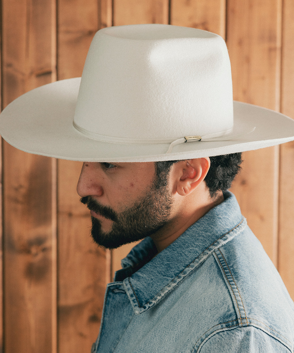 Man wearing a denim jacket and an ivory bull rider crown hat against a wooden background #color_silver grey