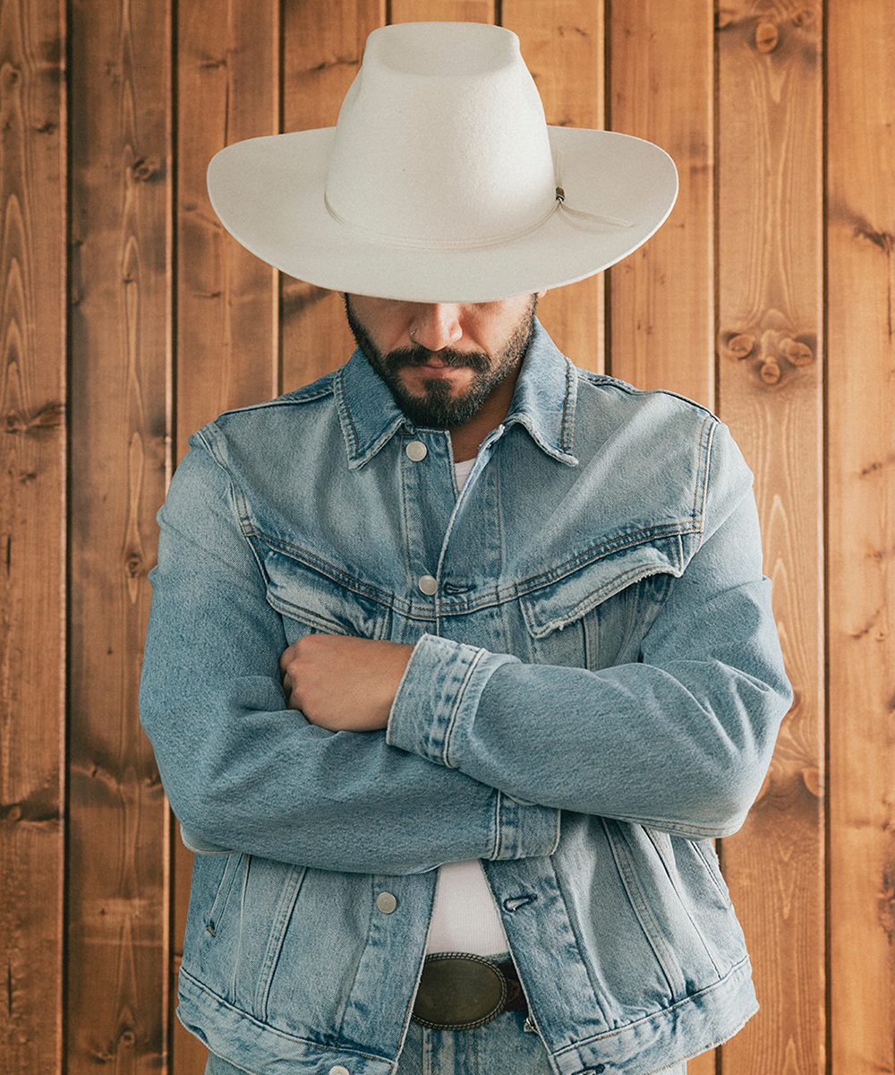 Man wearing a denim jacket and an ivory bull rider crown hat against a wooden background #color_silver grey