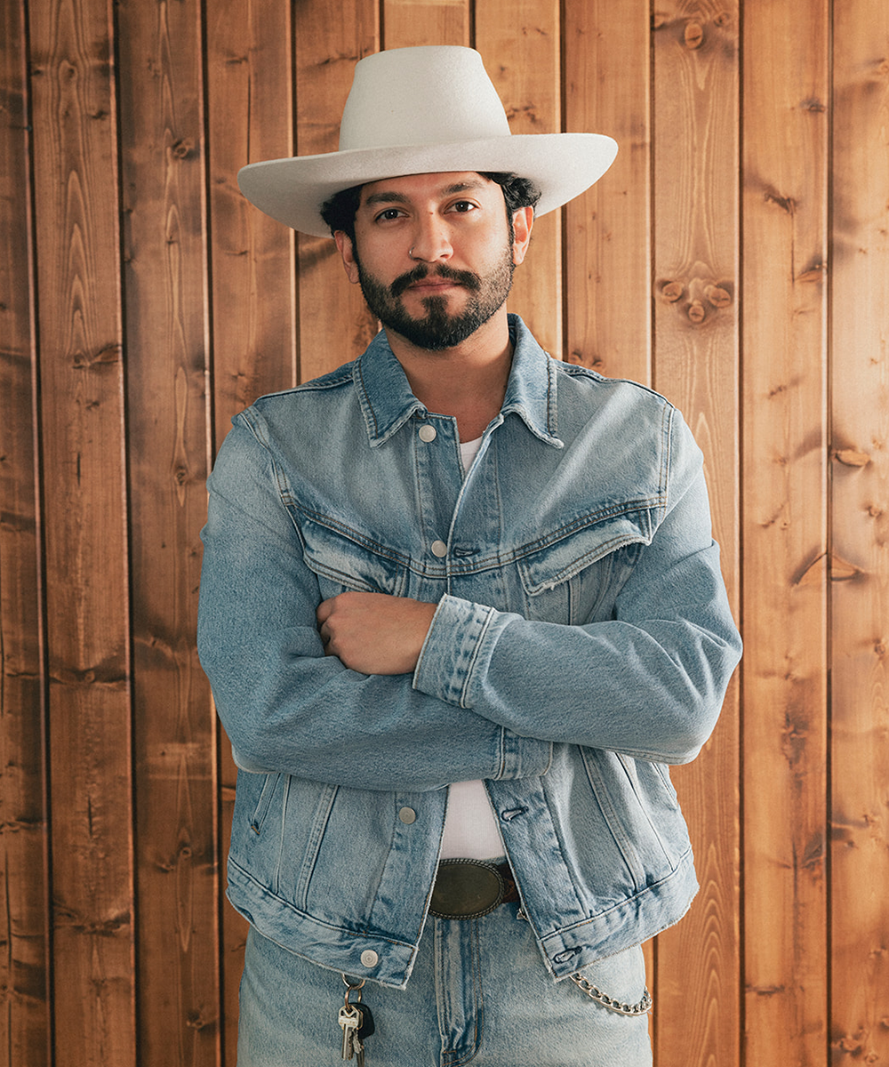 Man wearing a denim jacket and an ivory bull rider crown hat against a wooden background #color_silver grey
