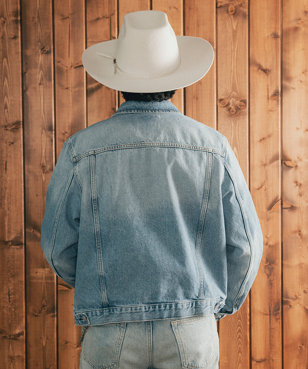 Man wearing a denim jacket and an ivory bull rider crown hat against a wooden background #color_silver grey