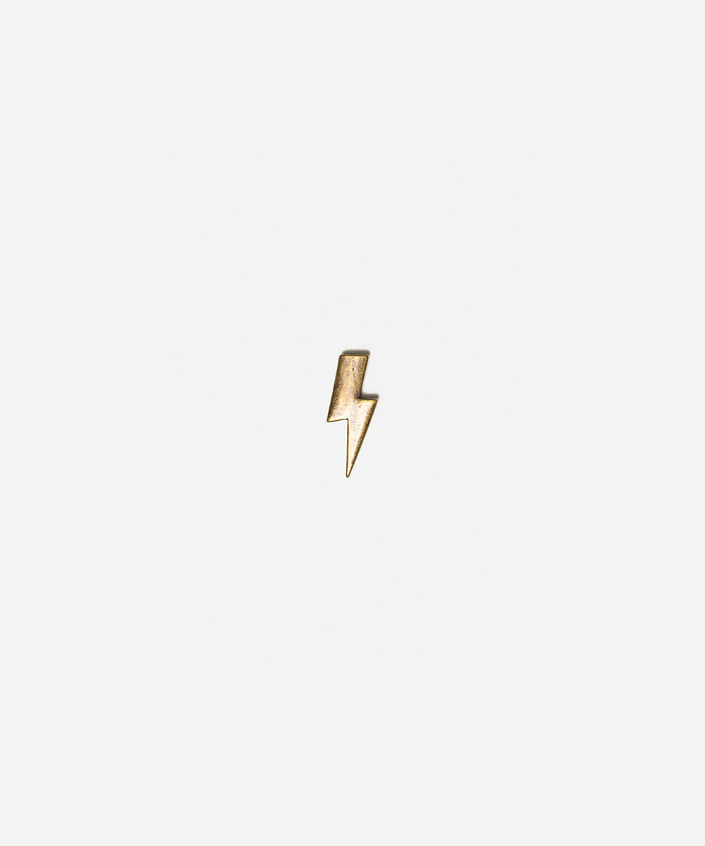 A small gold lightning bolt charm or pendant centered on a plain light gray background #color_anti gold