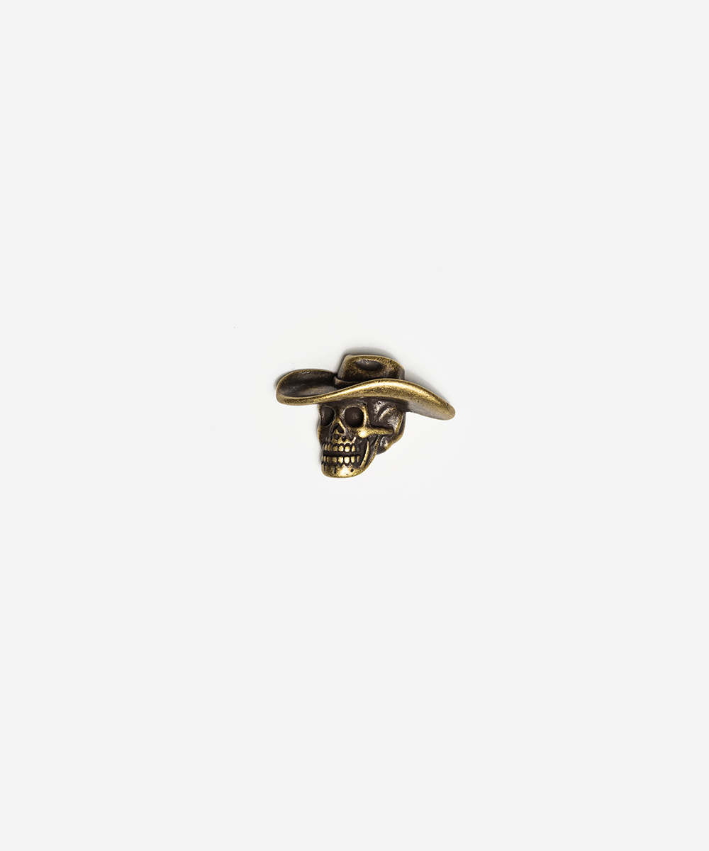 A small antique gold skull charm wearing a cowboy hat, centered on a plain light gray background #color_anti gold
